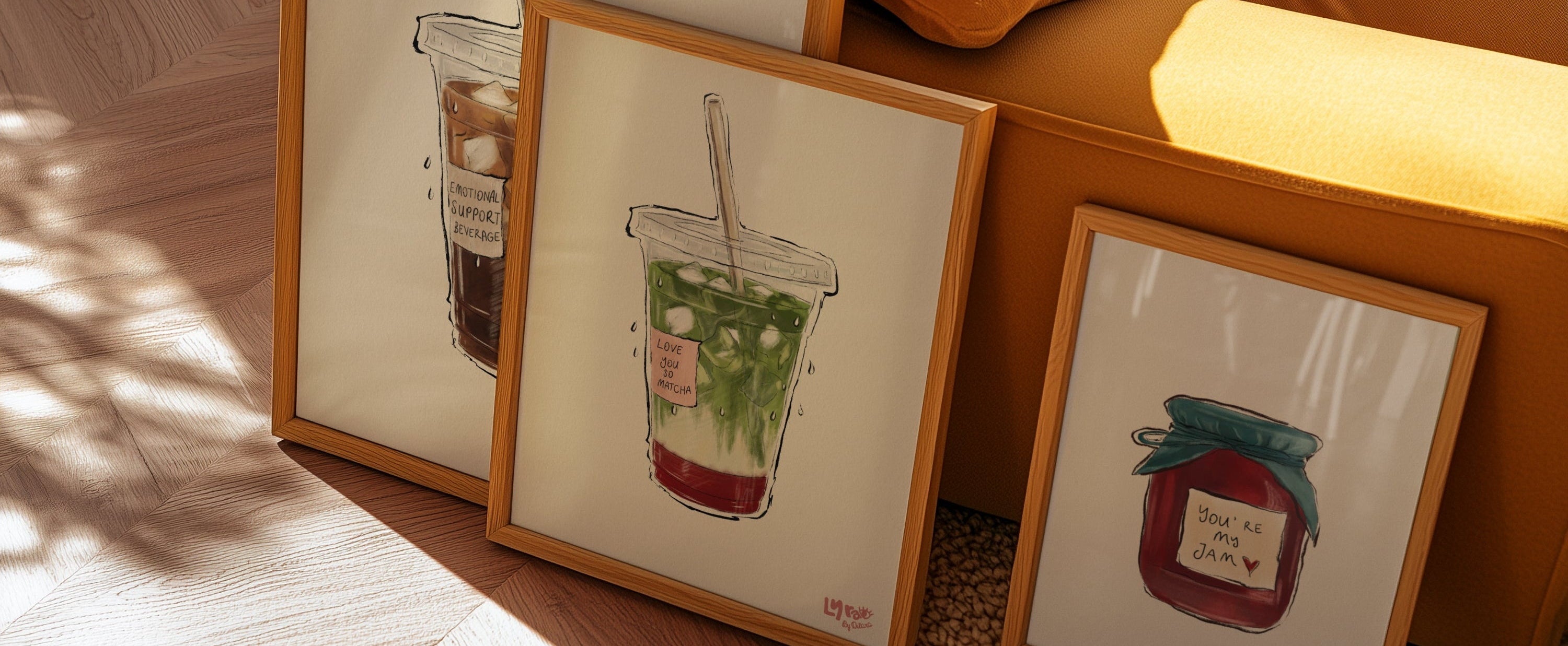Framed illustrations of drinks on a wooden floor next to a yellow couch.